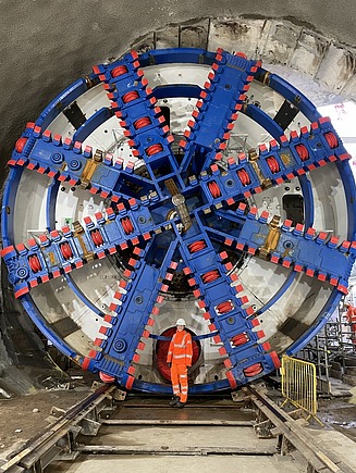 Junge Frau in Arbeitssschutzkleidung vor einer Tunnelbohrmaschine.