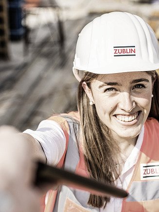 Foto von einer lächelnden Mitarbeiterin mit Bauhelm auf einer Baustelle