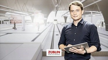 Foto von einem Mann, der in einem leeren Bahnhofsgebäude steht und lächelt 