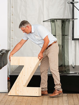 Person steht auf der Bühne, hat ein großes Z aus Holz in der Hand.