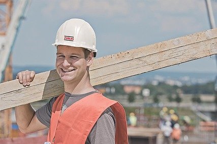 Foto von einem Mann mit Helm und Holzbrett auf der Schulter auf einer Baustelle