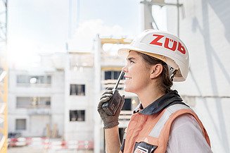 Foto von einer jungen Frau mit Helm und Funkgerät auf einer Baustelle 