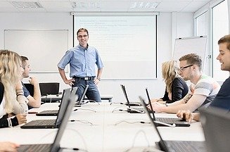 Foto eines Schulungsraums mit Teilnehmern am Laptop und einem Trainer 