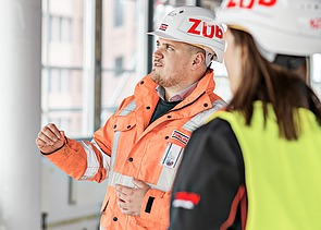 ZÜBLIN Mitarbeiter steht auf einer Baustelle und spricht mit Kollegin