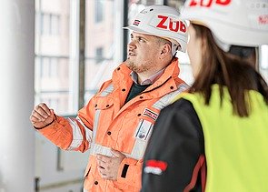 ZÜBLIN Mitarbeiter steht auf einer Baustelle und spricht mit Kollegin