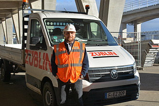 Junger Mann in Arbeitsschutzkleidung vor einem Auto mit ZÜBLIN-Branding