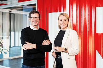 Two staff members in the office building are looking at the camera.