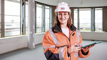 Junge Frau in Arbeitsschutzkleidung mit Tablet auf einer Baustelle.