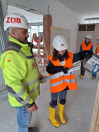 Mädchen in Arbeitsschutzkleidung und ZÜBIN Mitarbeiter in Arbeitsschutzkleidung messen Material.