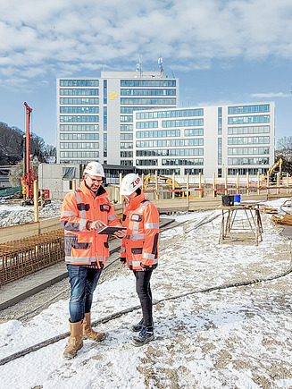 Bild von zwei Personen mit Bauhelm, die sich gerade auf der Baustelle besprechen.