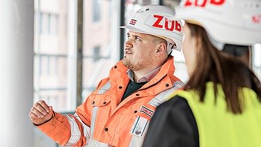 ZÜBLIN Mitarbeiter steht auf einer Baustelle und spricht mit Kollegin