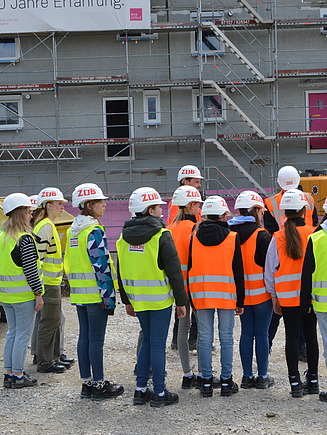 Kinder in Arbeitsschutzkleidung auf einer Baustelle, von hinten zu sehen