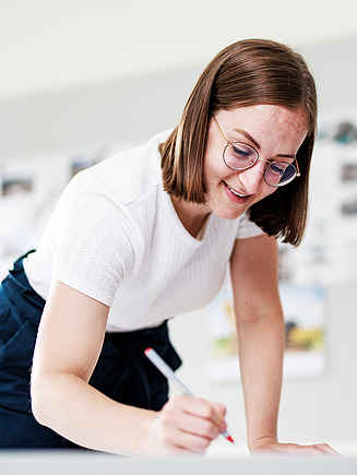 An apprentice is leaning over a desk and writing something.
