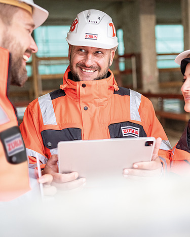 Four staff members on a building site; one person is pointing at something on a tablet.