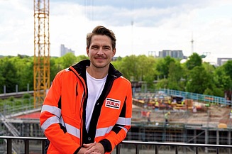 A young man in high-visibility workwear standing in front of a white wall
