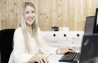 Foto von einer Frau, die im Büro vor dem Bildschirm sitzt und lächelt