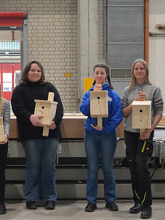 Mädchen stehen mit selbst gebauten Vogelhäusern aus Holz in der Produktionshalle von ZÜBLIN Timber.     