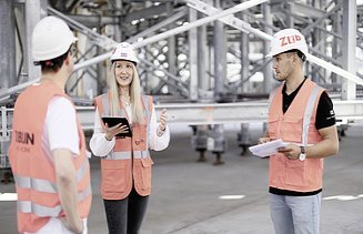 Foto von einer Frau, die mit zwei Kollegen auf der Baustelle redet 
