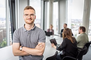 Besprechungssituation, ein Mitarbeiter im Vordergrund mit verschränkten Armen
