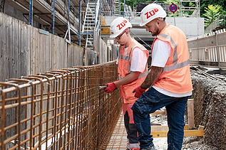 Zwei Mitarbeiter in Arbeitsschutzkleidung auf der Baustelle.