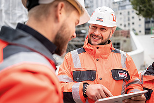 Nahaufnahme: Zwei Mitarbeiter in Arbeitsschutzkleidung auf einer Baustelle in einer Besprechungssituation