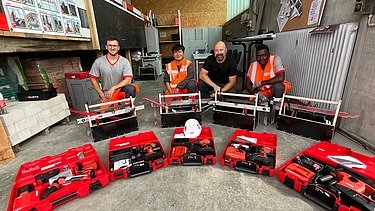 Oberpolier Mike mit drei Kollegen aus der Lehrlingsausbildung hinter offenen Werkzeugkoffern.