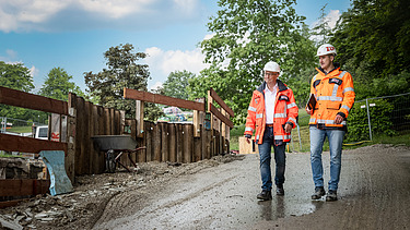 Zwei Mitarbeiter in Arbeitsschutzkleidung laufen über die Baustelle