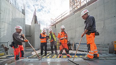 Fünf Personen in Arbeitsschutzkleidung auf der Baustelle am arbeiten