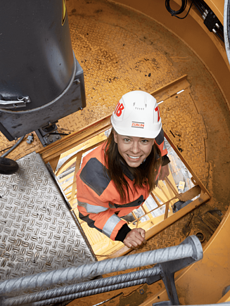 A woman climbs up a construction crane and looks into the camera.