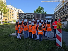Children in high-visibility clothing in front of the SEED construction site