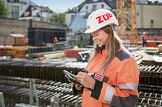 Foto von einer Bauleiterin, die gerade etwas auf ihrem Tablet bearbeitet und dabei auf auf der Baustelle steht