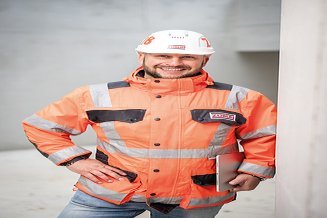 Mitarbeiter in Arbeitsschutzkleidung auf einer Baustelle, die Hand in die Seite gestemmt