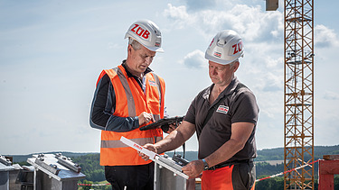 Two men in high-visibility workwear talking, with a crane in the background