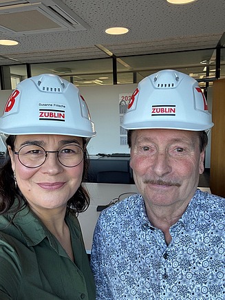 A selfie of two ZÜBLIN employees in the office wearing hard hats