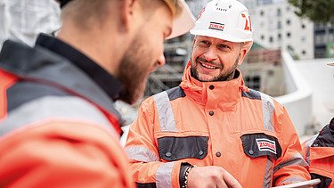 Nahaufnahme: Zwei Mitarbeiter in Arbeitsschutzkleidung auf einer Baustelle in einer Besprechungssituation