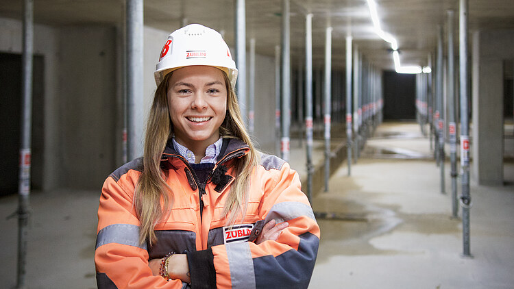 Bild einer jungen Bauleiterin in Arbeitskleidung, die in die Kamera lächelt
