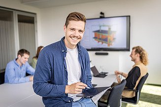 Foto von einem Mann in einem Schulungsraum, im Hintergrund arbeiten vier Mitarbeiter