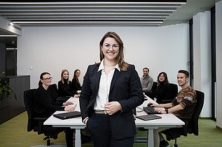 A ZÜBLIN employee standing in front of a conference table in the office, smiling at the camera
