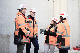 A photo of four ZÜBLIN employees standing in a circle on the building site, discussing something.