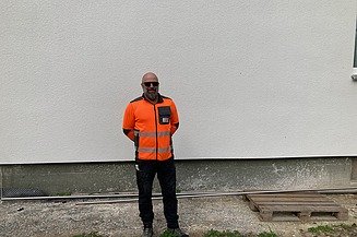 Oberpolier Mike in Arbeitskleidung vor einer Wand auf der Baustelle