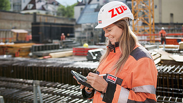Foto von einer Bauleiterin, die gerade etwas auf ihrem Tablet bearbeitet und dabei auf auf der Baustelle steht