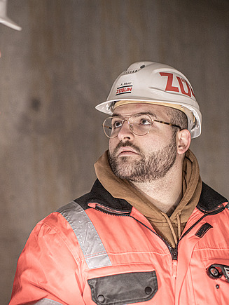 ZÜBLIN Mitarbeiter mit Bauhelm guckt einen weiteren Mitarbeiter an.
