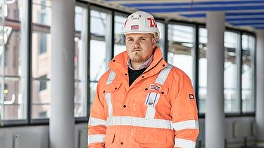ZÜBLIN Mitarbeiter steht mit Schutzausrüstung auf Baustelle und schaut in die Kamera