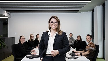 ZÜBLIN Mitarbeiterin, die vor Konferenztisch im Büro steht und in die Kamera lächelt