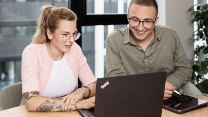 A young woman and a young man are looking at a laptop in a meeting room.