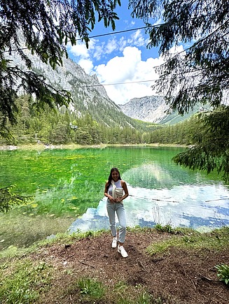 Junge Frau steht vor einem verspiegelten See, im Hintergrund die Berge