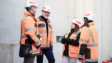 A photo of four ZÜBLIN employees standing in a circle on the building site, discussing something.