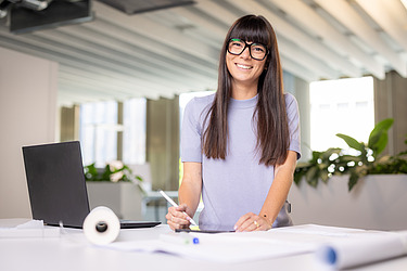 A photograph of a ZÜBLIN architect at her desk with drawings in front of her.