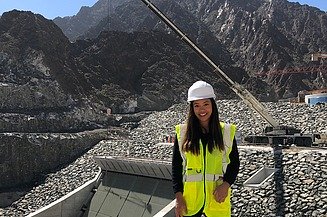Junge Frau mit Warnweste steht vor einem Bauwerk.