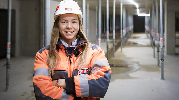 Bild einer jungen Bauleiterin in Arbeitskleidung, die in die Kamera lächelt